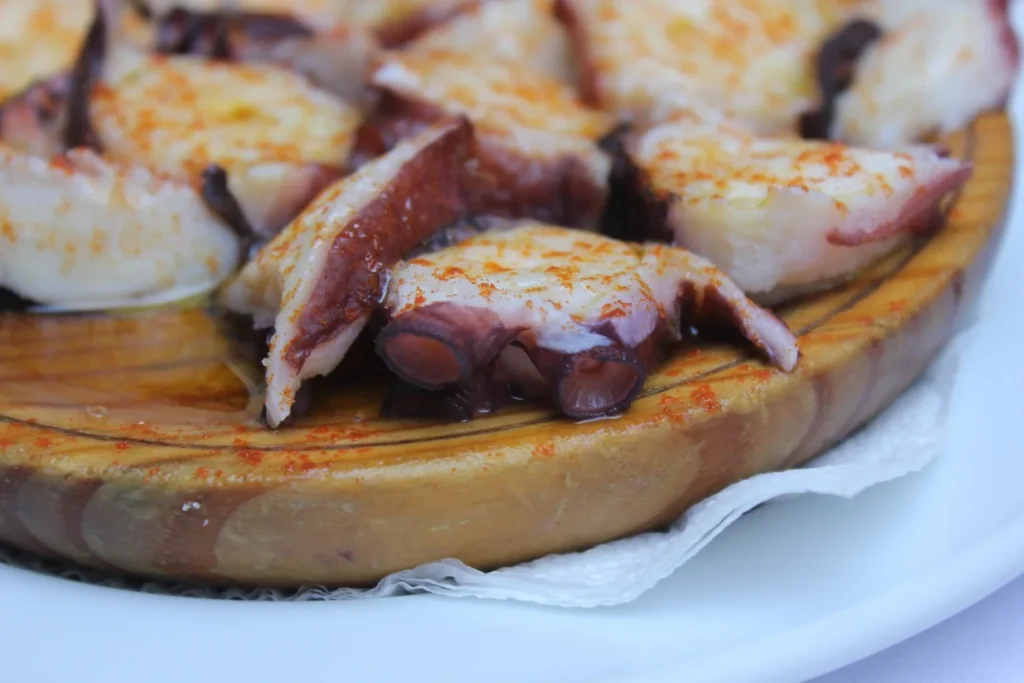Pulpo a la gallega con pimentón y aceite de oliva sobre plato de madera