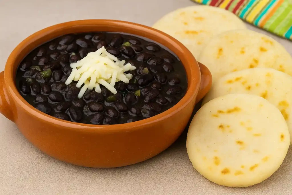 Caraotas negras con queso rallado y arepas, combinación criolla rica en proteína vegetal.