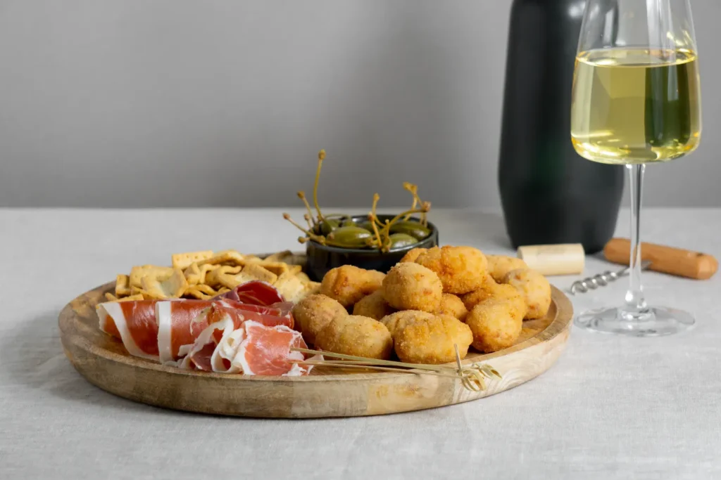 Croquetas doradas con jamón y aceitunas servidas con vino blanco en un bodegón de Margarita