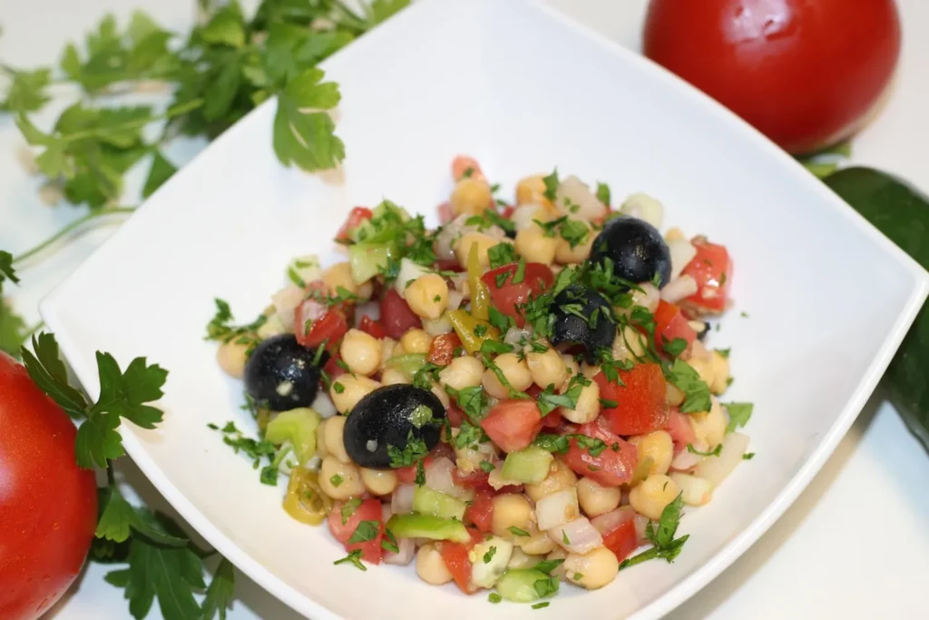 Ensalada fría de garbanzos con tomate, pepino y aceitunas, una opción ligera de proteína vegetal.